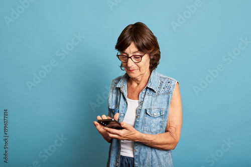 Latina senior woman using smartphone on blue studio background