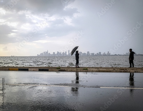 A couple enjoying the rainy season at Marine Drive, Mumbai, with monsoon waves and a wet promenade