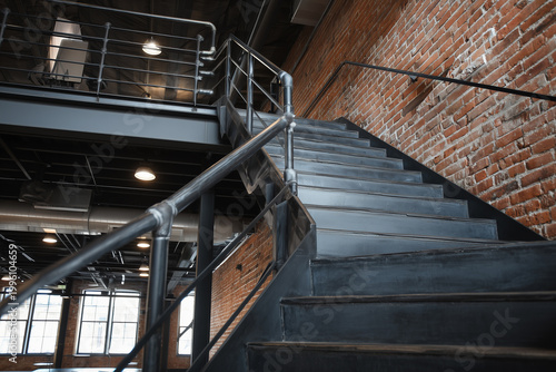 Metal staircase with raw steel steps leading to upper level in modern interior space with exposed brick wall and industrial design elements