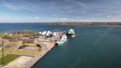 Aerial footage of industrial oil terminal located along coastline with large storage tanks, docked tanker ships. Aerial view of an industrial oil terminal and tanker ships at port, Fredericia, Denmark