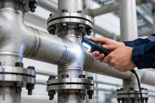Foto Industrial worker inspects metal pipes with a flashlight, checking for leaks or