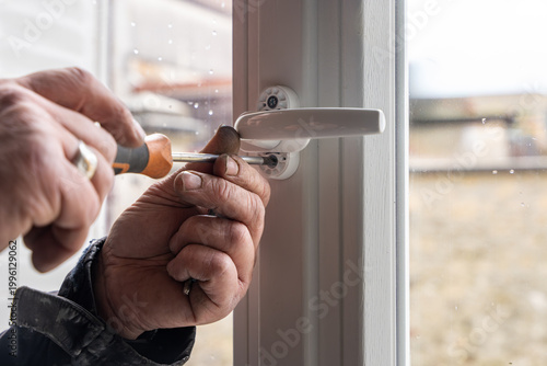 Foto Gros plan sur les mains d'un artisan utilisant un tournevis pour ajuster avec précision la poignée d'une fenêtre en PVC blanc lors d'une installation de menuiserie