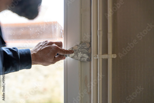 Schilderij op canvas Un artisan utilise un couteau de peintre pour appliquer avec précision de l'enduit de lissage sur l'encadrement d'une fenêtre, près de tuyauteries apparentes