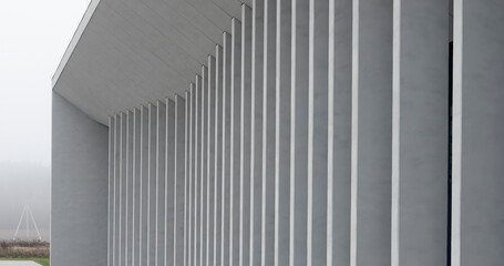 Modern gray building facade with tall vertical columns. Clean minimalist architecture under an overcast sky. Corporate exterior for office, museum, or public design..
