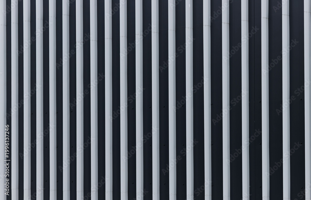 Obraz premium Vertical metal facade with repeating light and dark stripes. Modern building exterior detail with abstract architectural pattern. Suitable for