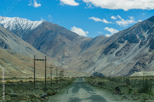 A concrete road towards beautiful rocky mountains and blue sky with peaks of Himalaya, Leh, Ladakh, Jammu and Kashmir, India