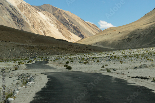 A concrete road towards beautiful rocky mountains and blue sky with peaks of Himalaya, Leh, Ladakh, Jammu and Kashmir, India