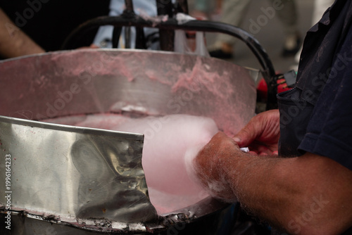 Horizontal photo close up. Male hands makes pink cotton candy in machine. Man seller in street pastry shop counter sells sweets. Independence day, May 26, city festival Tbilisoba, fair, sale concept