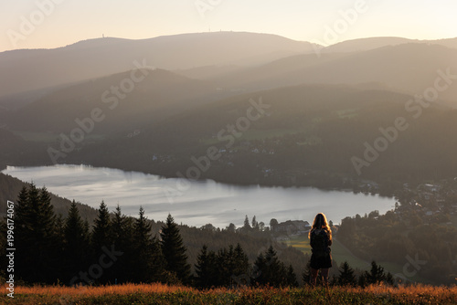 Ein ruhiger Moment in der Natur: Eine Person genießt den Sonnenuntergang über dem Titisee im Schwarzwald und blickt über die sanften Hügel und Wälder im goldenen Licht der Abendstunden.