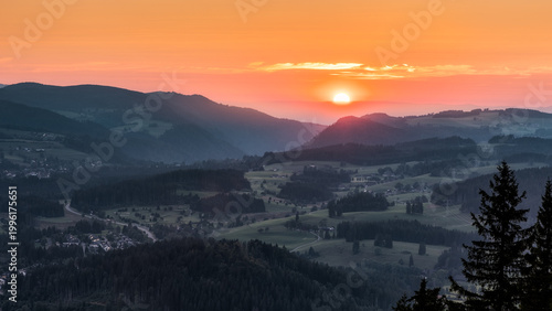 Atmosphärische Landschaft im Schwarzwald bei Sonnenuntergang. Die tief stehende Sonne taucht die sanften Hügel und Täler in warmes Licht, während sich die Landschaft in weichen Farbverläufen und ruhig