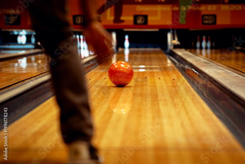 фотографія Jugador lanzando una bola de bolos naranja por la pista.