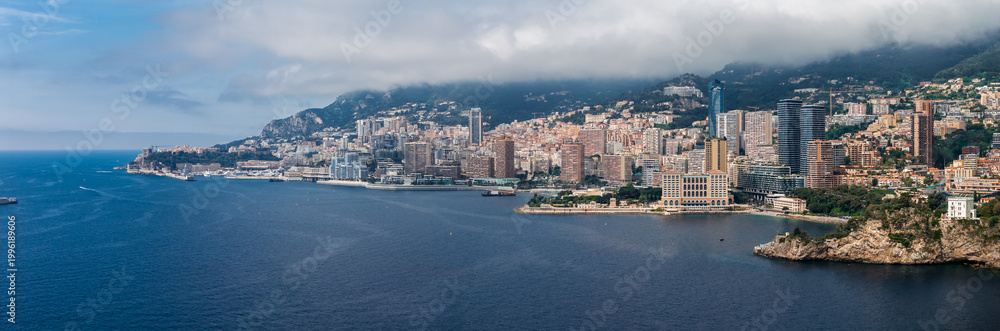 Φωτογραφία Aerial view of Monaco with Port Hercule and Monte Carlo, curved harbor walls, rocky headlands, high rise towers, terraced apartments, and cloud covered hills along the coast
