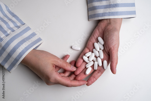 Close-up of woman's hands holding white pills or vitamin supplements above white table.