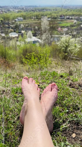 Feet resting on green grass with a scenic view of houses and trees in the distance