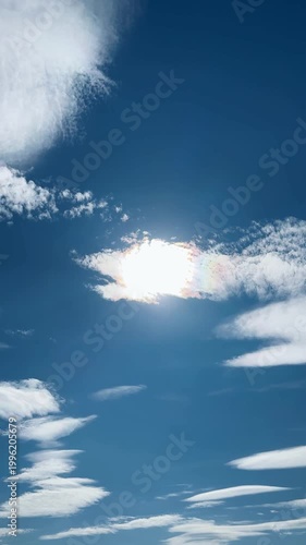 Bright sun shines through fluffy clouds on a clear blue sky
