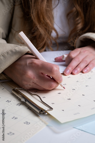 Close-up of woman's hands writing in calendar and marking dates for project planning