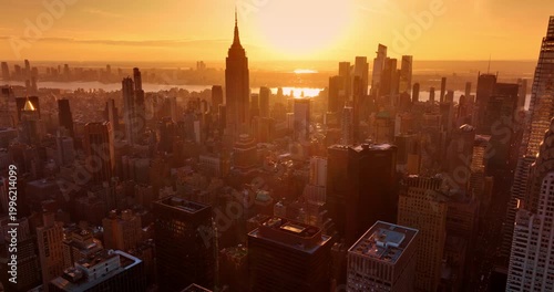 Golden hour in modern New York, USA. Orange light dazzles the dense urban panorama of Manhattan. Aerial view.