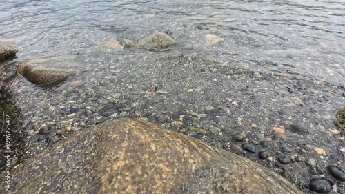 Haines - Alaska - USA - April 21 - Close up to a rocky shoreline with clear water. The rocks are rounded and smooth, and the water is clear and translucent. The scene is serene.