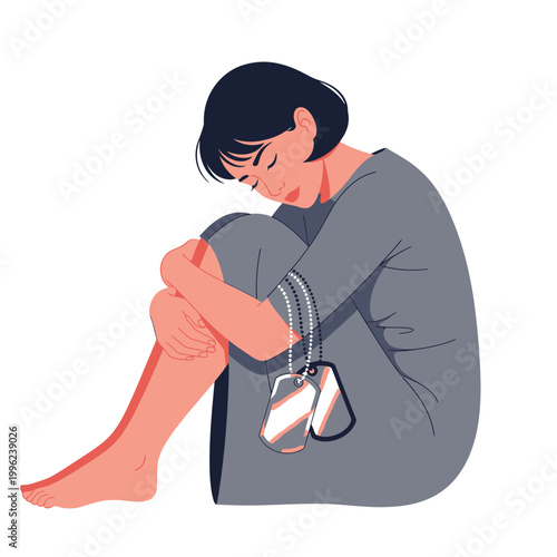 Woman sits with her knees pulled to her chest while holding military identification tags in mourning.