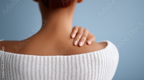Stress relief concept, A woman with short hair and polished nails touches her bare shoulder, wearing a white knitted off-shoulder sweater against a soft blue background.