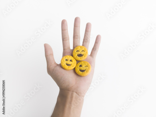 Three happy smiling and winking chocolate emoji biscuits on open hand palm over white background.
