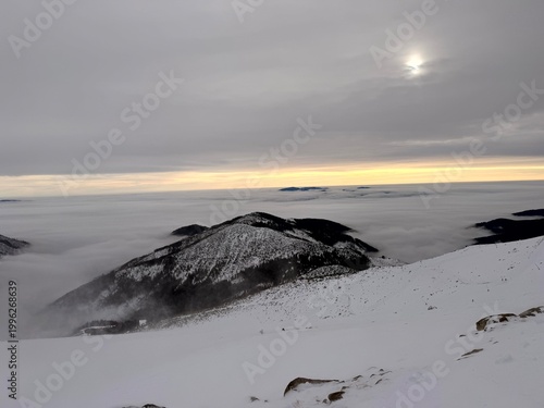 Minimalist snowy mountain peaks above clouds with soft sun and moody sky