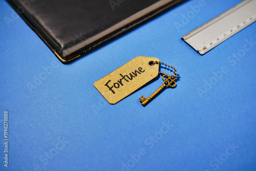 A vintage golden key with a tag reading 'Fortune' rests on a vibrant blue surface next to a notebook and ruler, symbolizing opportunity and success.