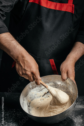 Baker mixing elastic dough in metal bowl with spoon homemade baking process