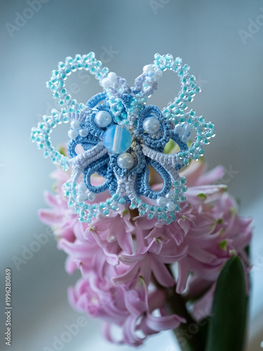 Handmade butterfly brooch, made using tatting technique with blue beads and moonstone, photographed on a on a pink flower.