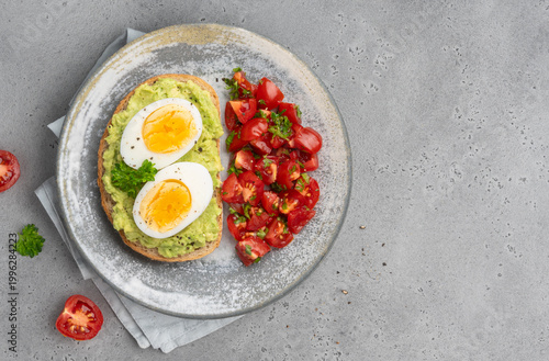 Foto Avocado toast (sandwich or bruschetta) with boiled egg served with tomatoes salad on grey ceramic plate