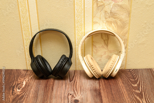black and beige headphones standing vertically on a wooden table against light wallpaper