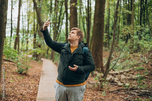 Sad blonde man got lost and could not find an internet connection on phone while hiking alone in the forest. Male explorer looking for connection to the internet or using gps navigator app on phone