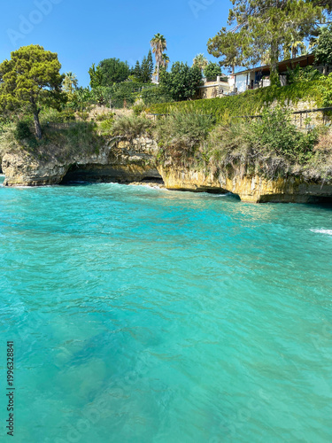 Scenic view of turquoise sea with rocky coastline and green vegetation. Summer coastal landscape with clear water, sunny weather and natural seaside atmosphere.