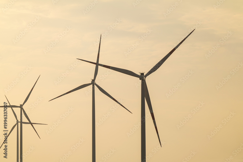 Fototapeta premium Wind turbines stand tall against a hazy sunset sky in a renewable energy field