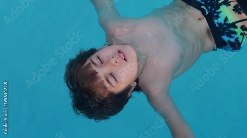 Happy Child relaxing in blue swimming pool. Boy with dark hair floats on his back in clear, bright blue water. His eyes are closed in peaceful relaxation. Serene, calm mood. Tranquility and summer.