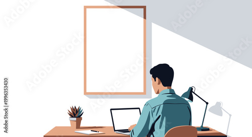 A man working on a laptop at a desk with a blank frame on the wall.