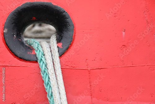 Fotografi Red boat hull featuring a weathered black hawsehole, securely holding two thick,