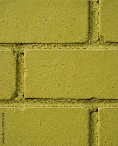 Close-up texture of a rough yellow painted brick wall. Macro detail of urban masonry, porous bricks, and mortar lines. Mustard green building exterior background with copy space.