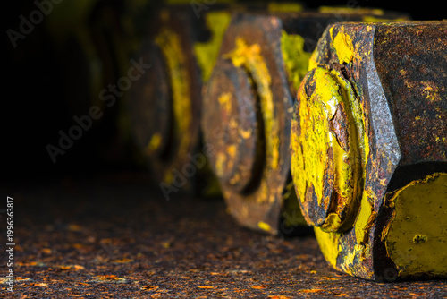 Close-up of thick old bolts with nuts on a rusty steel surface, in dark industrial environment