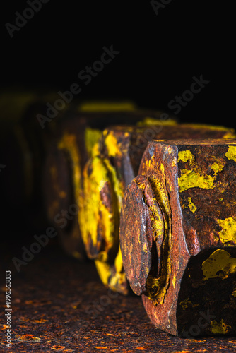 Close-up of thick old bolts with nuts on a rusty steel surface, in dark industrial environment