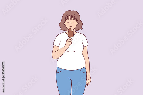 A young plus-size woman enjoys eating a chocolate-covered ice cream bar, treating herself to a delicious and cold sweet snack indoors.