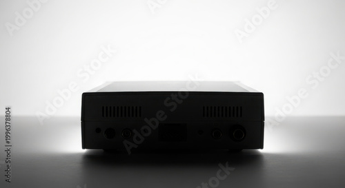 Back view of a sleek, dark electronic device with illuminated ports and ventilation slits, silhouetted against a bright white background.