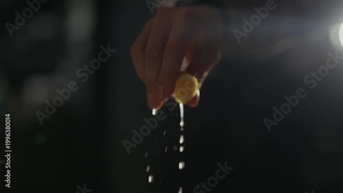 Hand squeezes lemon, juice drips down. Light flares behind, casting shadows. Close-up, slow-motion, captures freshness. Use for food, health, or natural product visuals