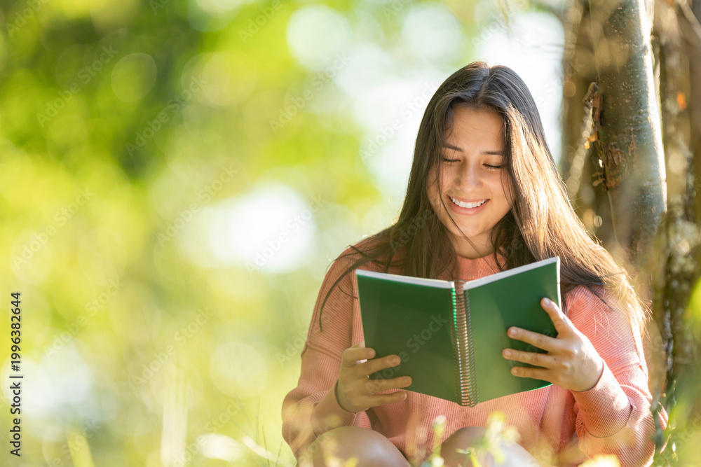 Fototapeta premium Young woman smiling while reading book outdoors in nature