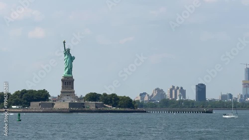 Long-distance view of the Statue of Liberty across open harbor water with soft city skyline in the background. Minimal peaceful composition emphasizes scale, space, and iconic American scenery.