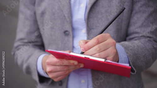Young man in suit making notes on paper, working outside. Close up. Real time