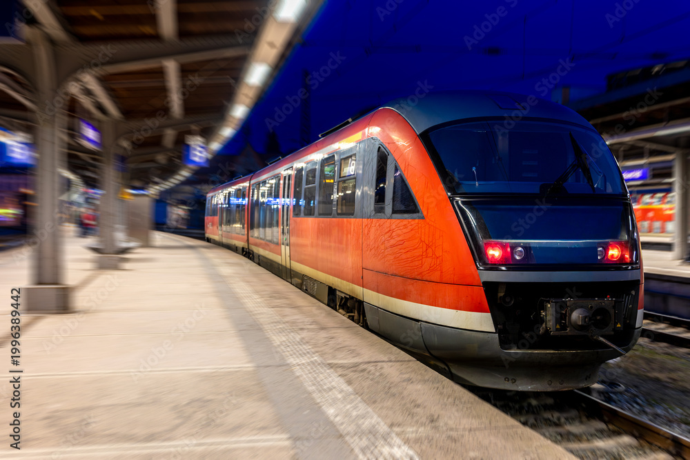 Fototapeta premium Red train arrives at night station. Modern passenger transport at the railway platform.