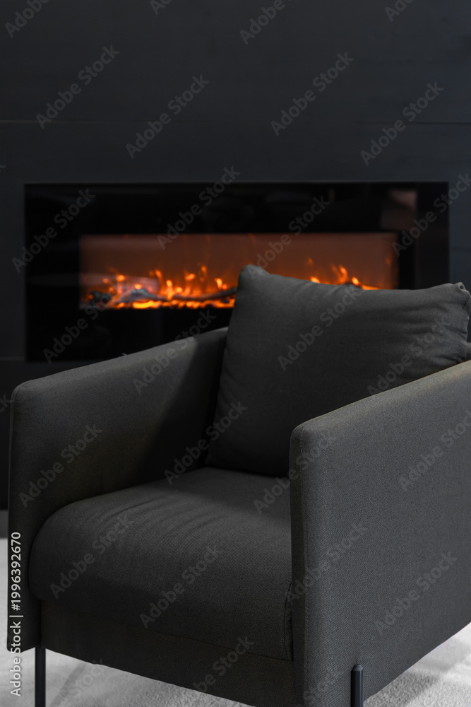 Fototapeta premium Elegant dark grey armchair near fireplace. Modern home relaxation area interior design.