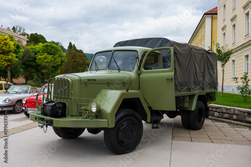 Rogaska Slatina, Slovenia. Military green vintage truck parked on a city street with classic cars and trees in the background