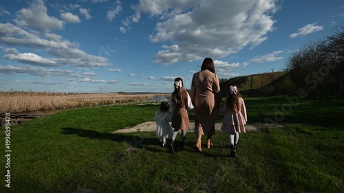 A Mother and Her Three Daughters Enjoy a Peaceful Walk Together in Nature, Holding Hands Along a Grassy Path on a Beautiful Sunny Day